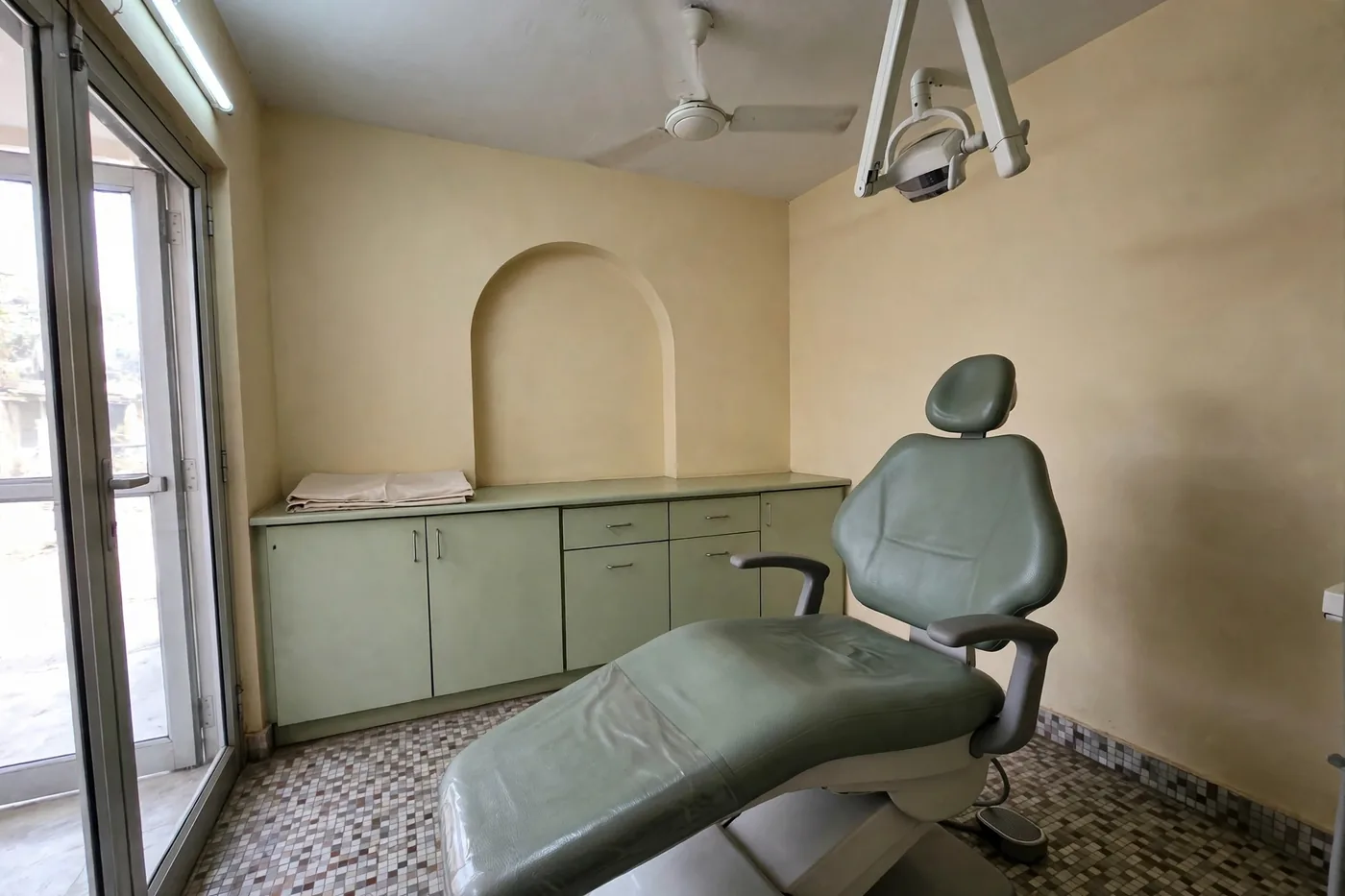 An empty treatment room with the dental chair ready, cabinets and the arched wall behind