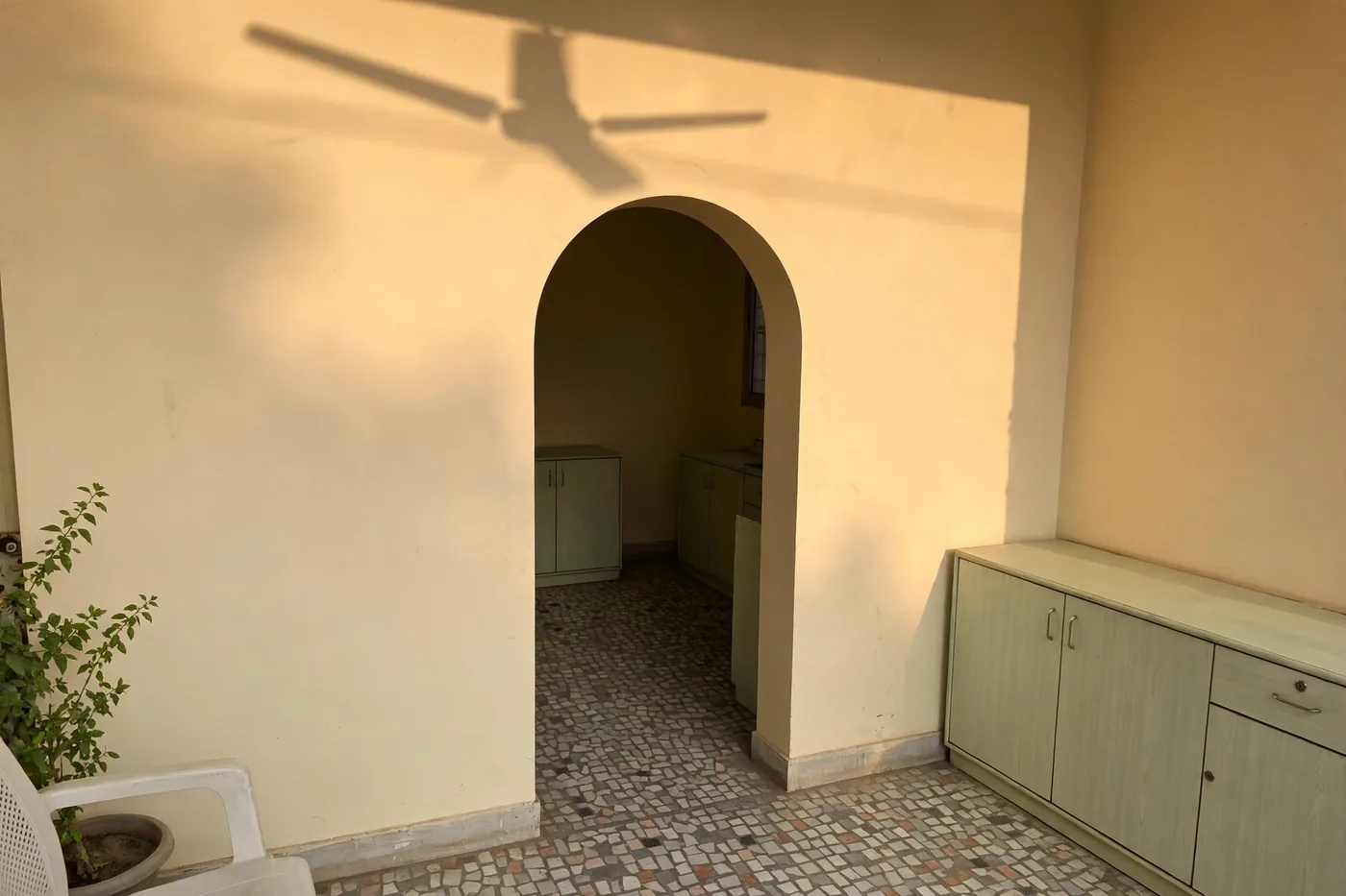 Late-afternoon sunlight and the ceiling fan's shadow across the arched wall